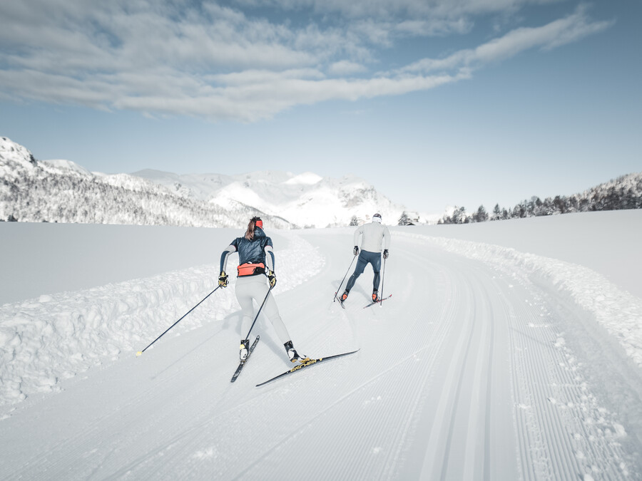 Zwei Menschen fahren auf einer präparierten, verschneiten Loipe Langlauf, im Hintergrund sind Berge zu sehen. - Hotel Steinerhof
