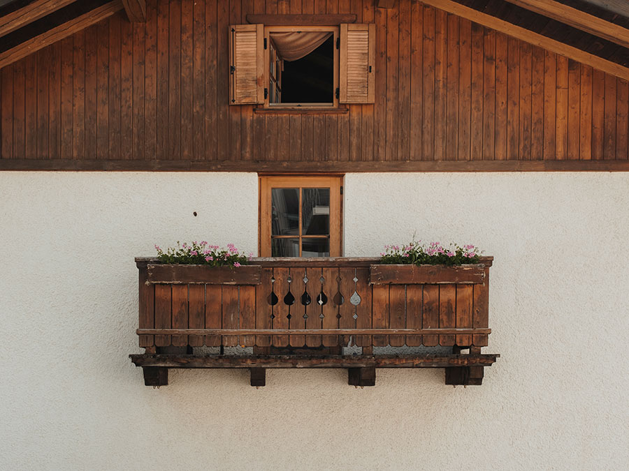 Holzbalkon mit Blumenkästen unter einem Fenster an einem rustikalen, weiß-braunen Gebäude. - Hotel Steinerhof