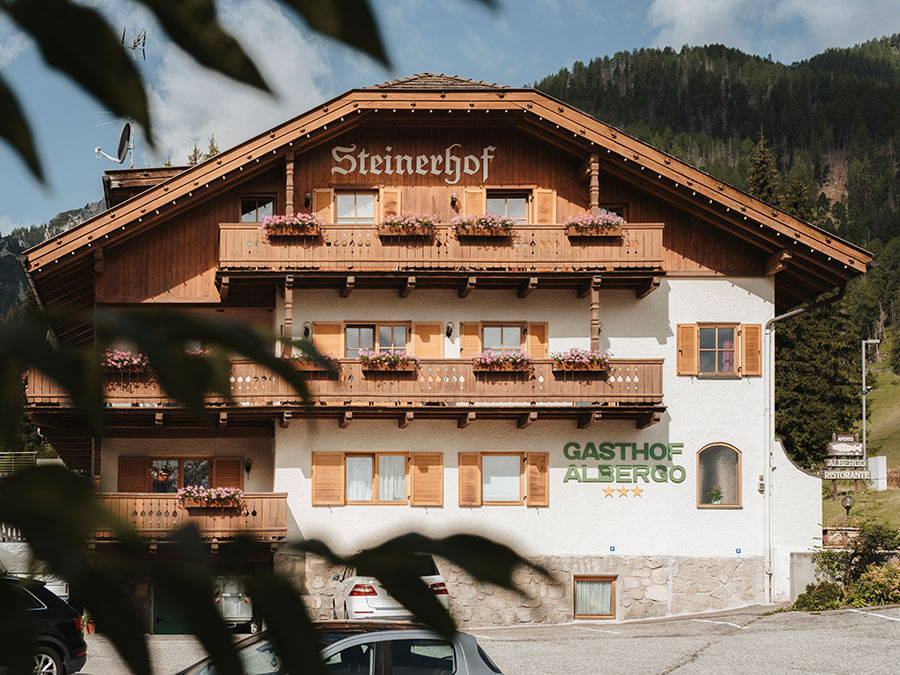 Das alpine Gästehaus „Steinerhof“ aus Holz mit Balkonen, Blumenkästen und der Bergkulisse im Hintergrund. - Hotel Steinerhof