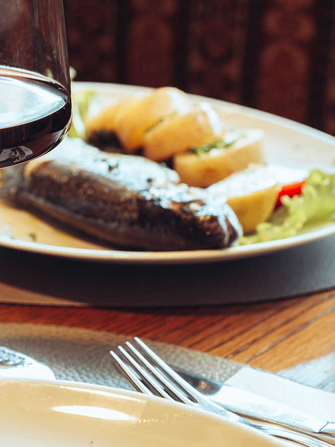 Ein Glas Rotwein vor einem Teller mit Wurst, Brot und Salat auf einem Holztisch. - Hotel Steinerhof