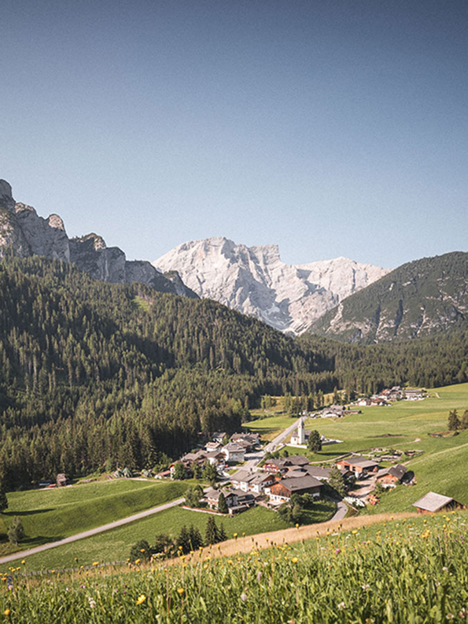 Ein kleines Dorf, eingebettet in ein grünes Tal, mit Kiefernwäldern und hohen, schneebedeckten Bergen im Hintergrund. - Hotel Steinerhof