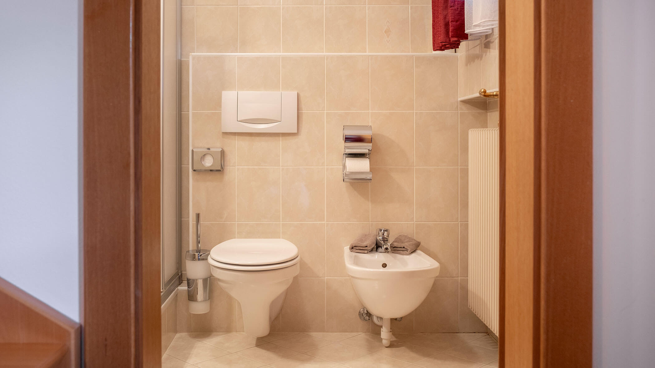 Ein Badezimmer mit Toilette, Bidet, Toilettenpapier sowie beigen Fliesen an Wänden und Boden. - Hotel Steinerhof