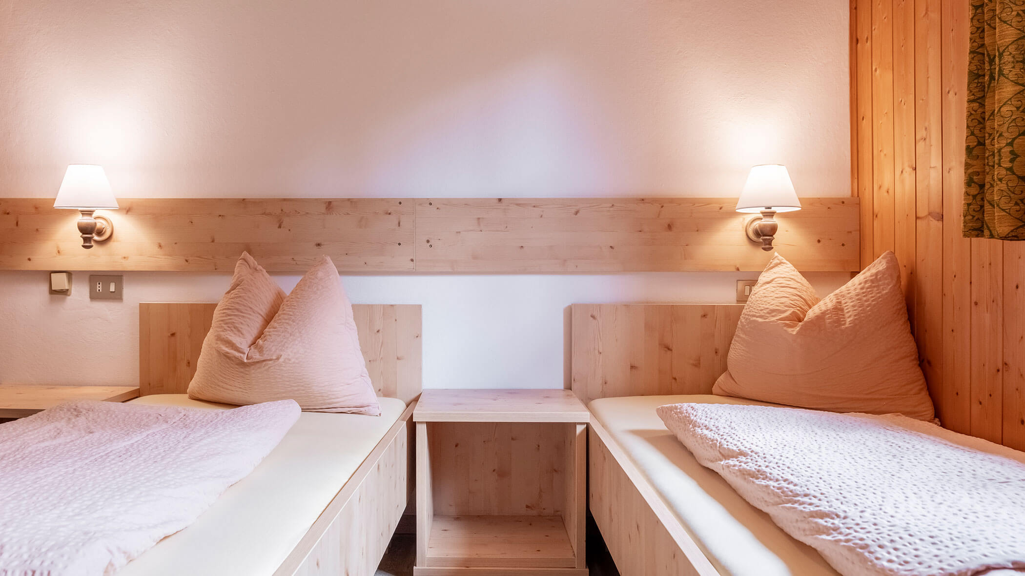 Zwei Einzelbetten mit beiger Bettwäsche, Kopfenden aus Holz und Wandlampen in einem gemütlichen, minimalistisch eingerichteten Zimmer. - Hotel Steinerhof