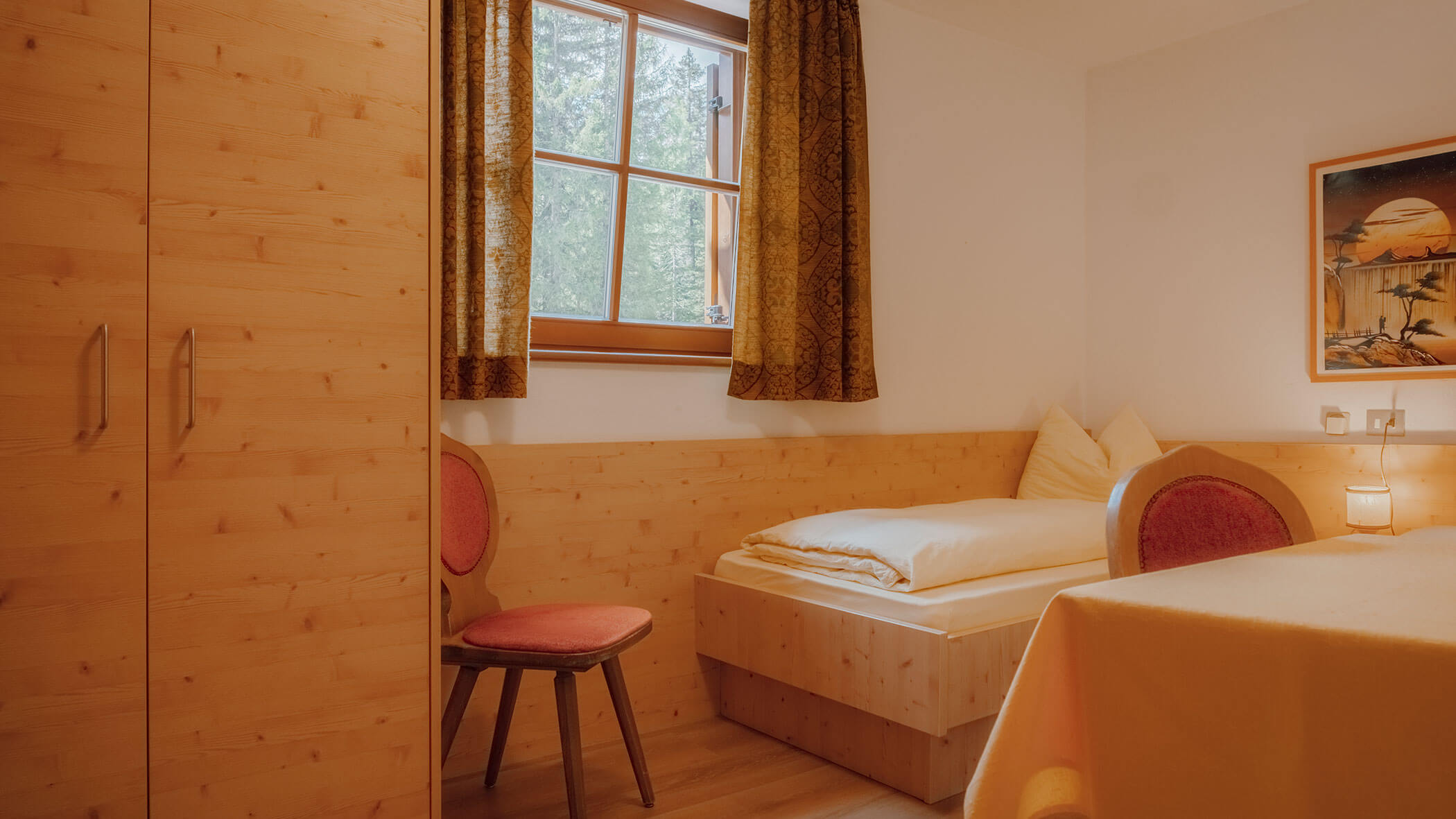 Gemütliches Schlafzimmer aus Holz mit einem Einzelbett, einem Kleiderschrank, einem Stuhl, einem Fenster und einer Einrichtung in warmen Gelbtönen. - Hotel Steinerhof