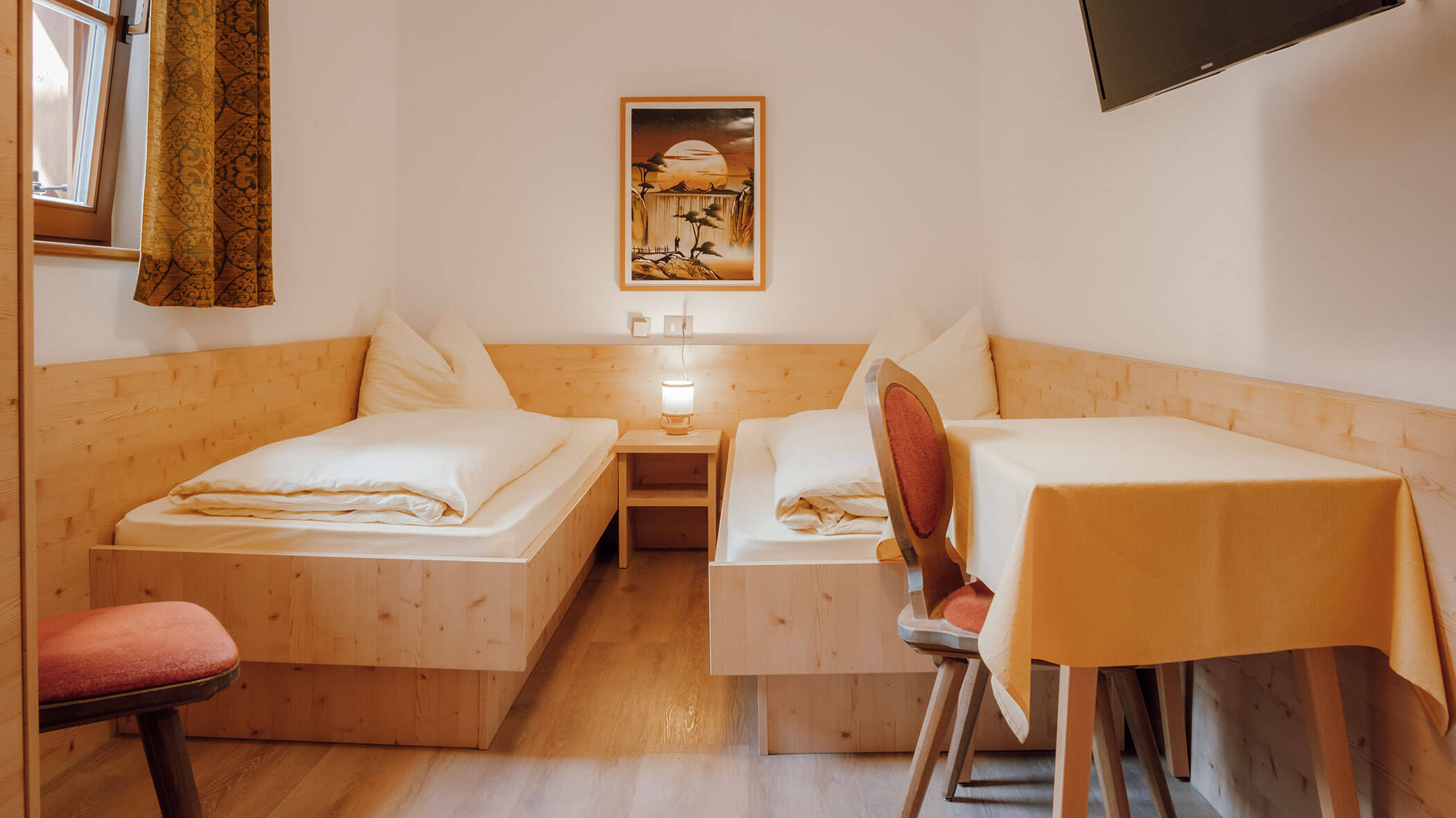 Gemütliches Zimmer mit zwei Einzelbetten, einem kleinen Tisch mit Stühlen, einer Lampe und einem an der Wand montierten Fernseher. - Hotel Steinerhof