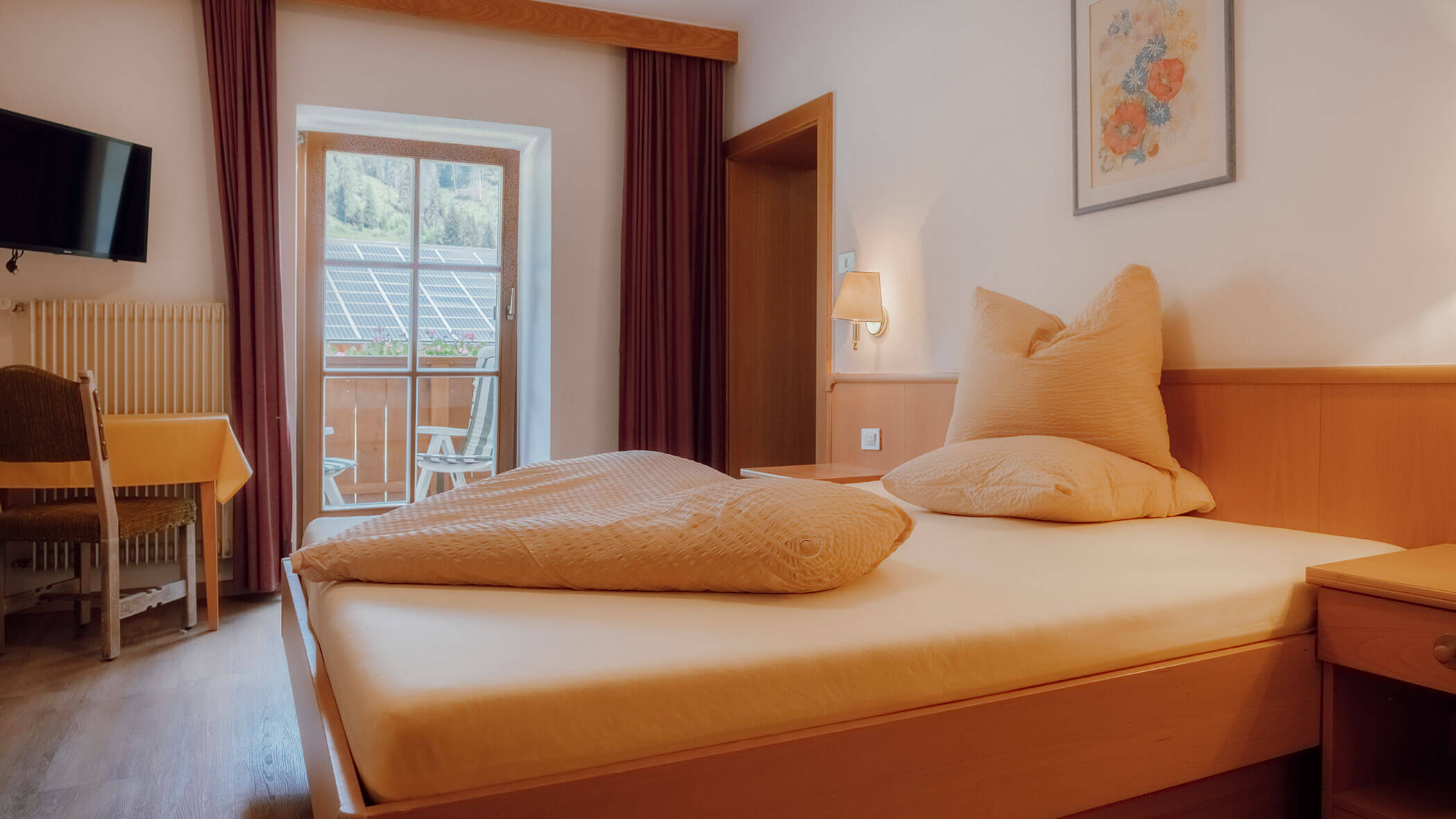 Gemütliches Hotelzimmer mit einem Einzelbett, Fernseher, Schreibtisch und Balkon mit Blick auf Bäume und Solaranlagen. - Hotel Steinerhof