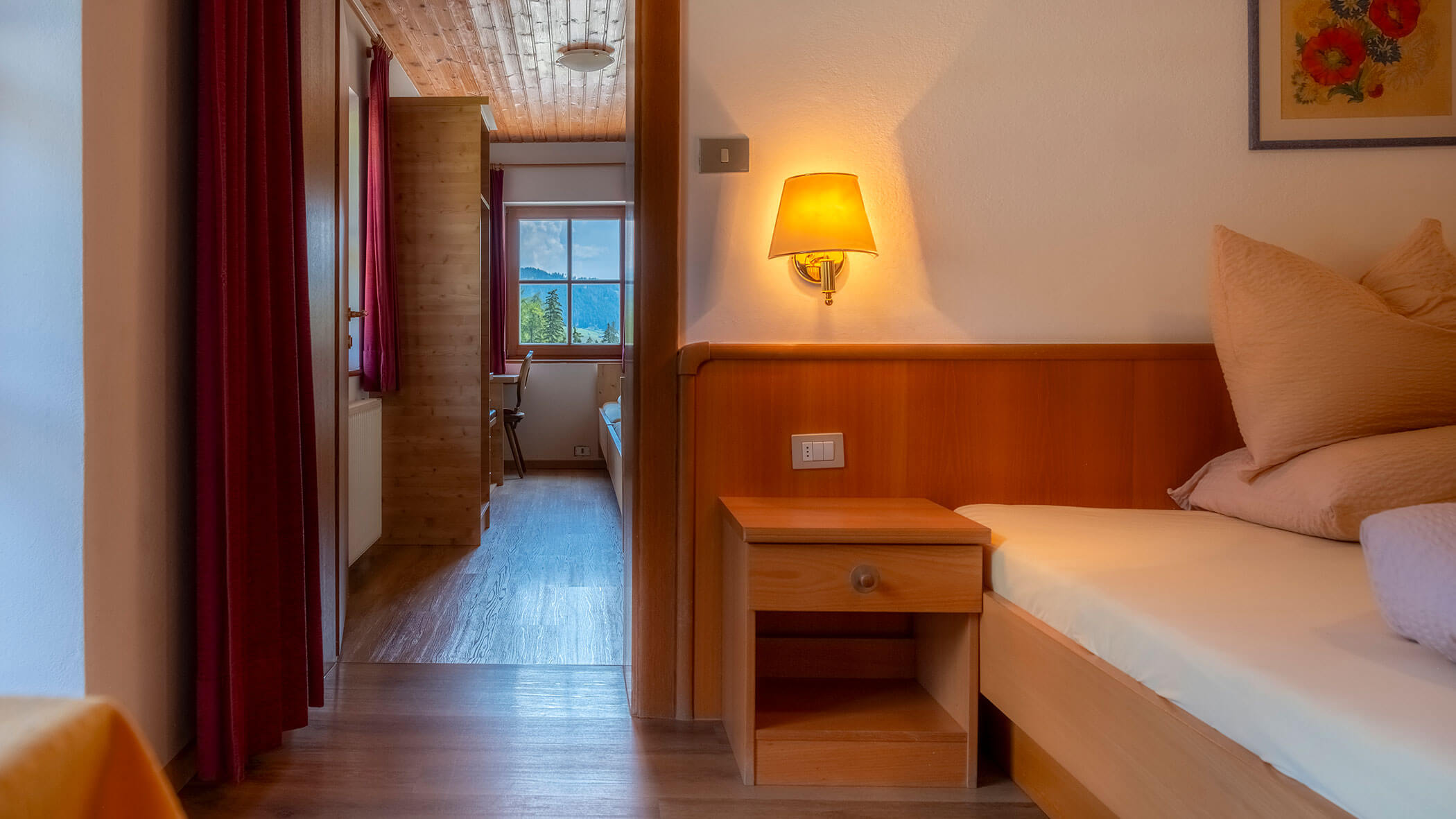 Gemütliches Schlafzimmer mit einem Einzelbett, einer Lampe und einem Flur, der zu einem Fenster mit malerischem Blick ins Freie führt. - Hotel Steinerhof