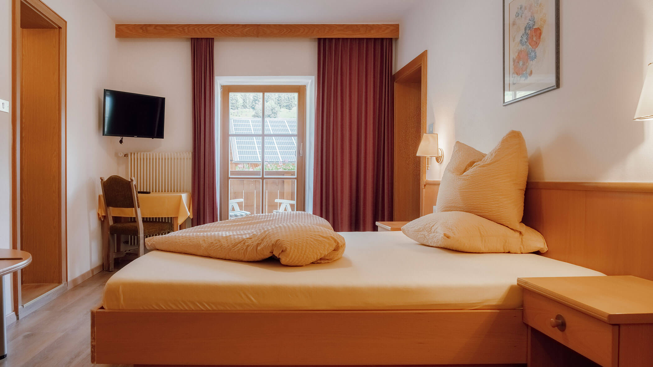 Gemütliches Hotelzimmer mit einem Doppelbett, Balkon, Fernseher, Schreibtisch und Sonnenlicht, das durch das Fenster hereinströmt. - Hotel Steinerhof