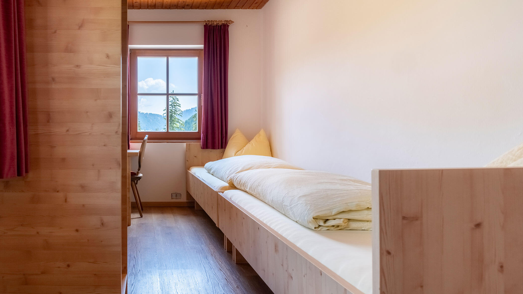 Einfaches Schlafzimmer mit einem Einzelbett, Holzmöbeln, einem Fenster mit lila Vorhängen und Tageslicht. - Hotel Steinerhof