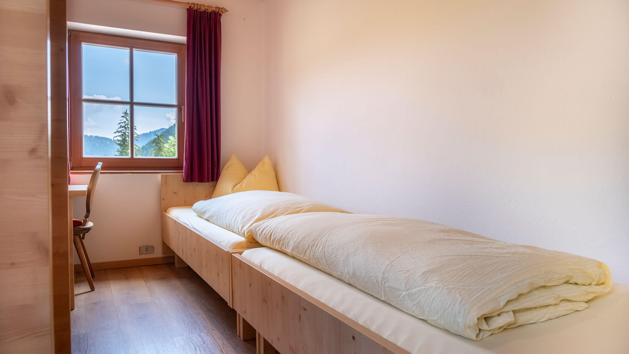 Kleines Schlafzimmer mit einem Einzelbett, gelber Bettwäsche, einem Schreibtisch, einem Stuhl und einem Fenster mit Blick auf die Berge. - Hotel Steinerhof