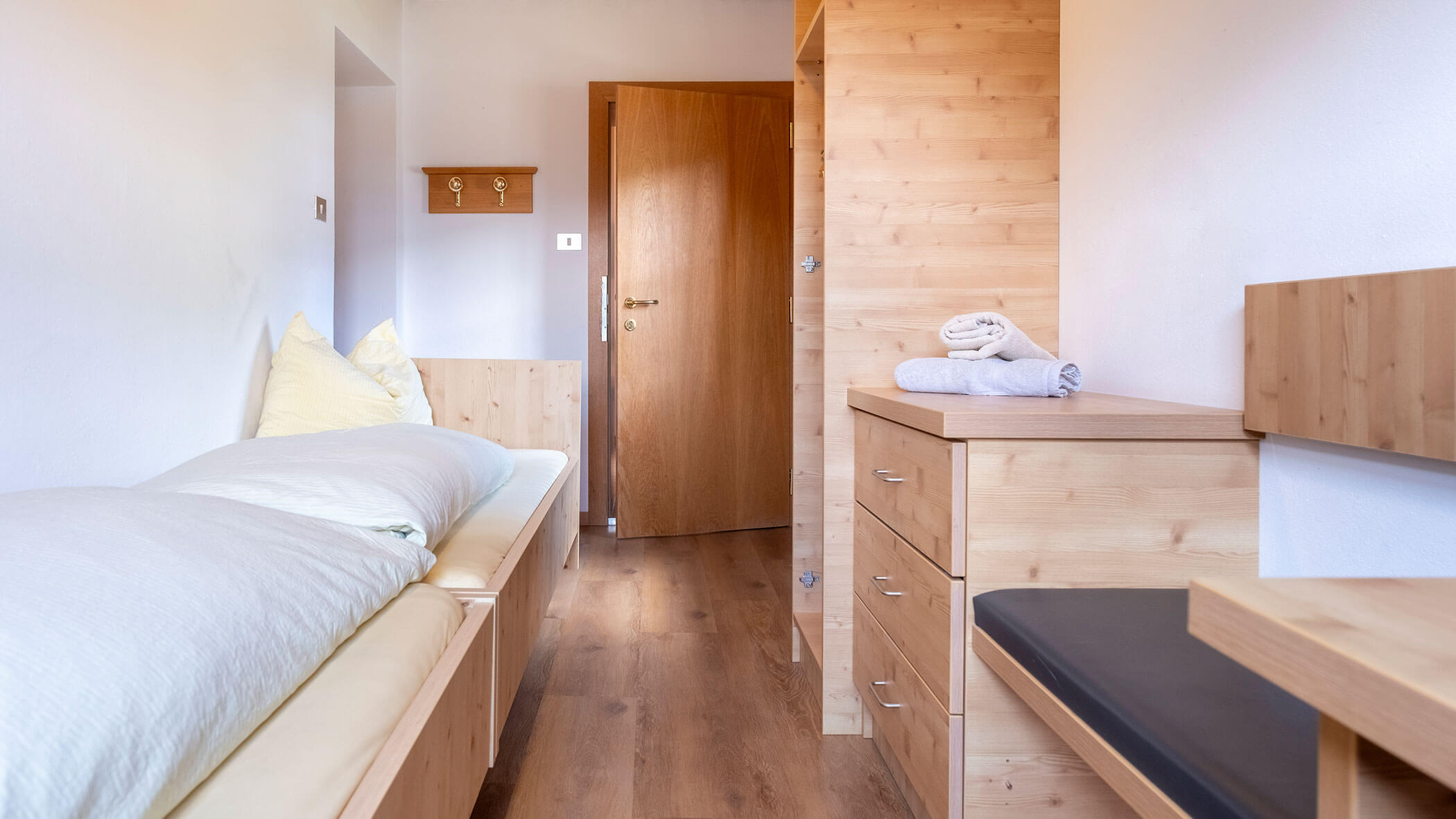 Ein kleines Schlafzimmer mit einem Einzelbett, Holzmöbeln, gefalteten Handtüchern und einer offenen Tür. - Hotel Steinerhof