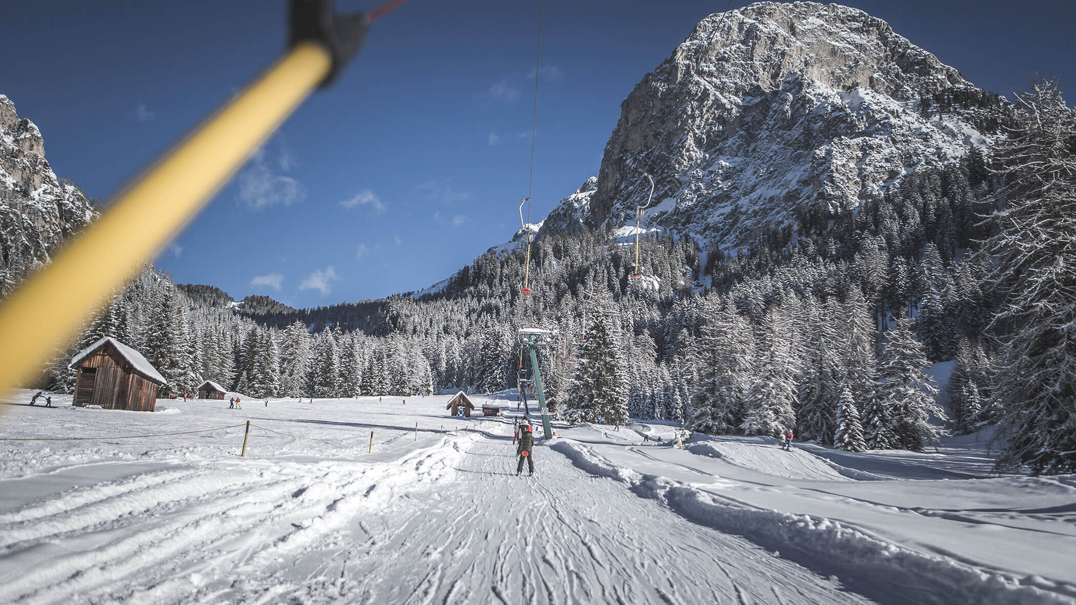 Ein Skifahrer, der einen Skilift in einer verschneiten Berglandschaft mit Bäumen und Holzhütten benutzt. - Hotel Steinerhof