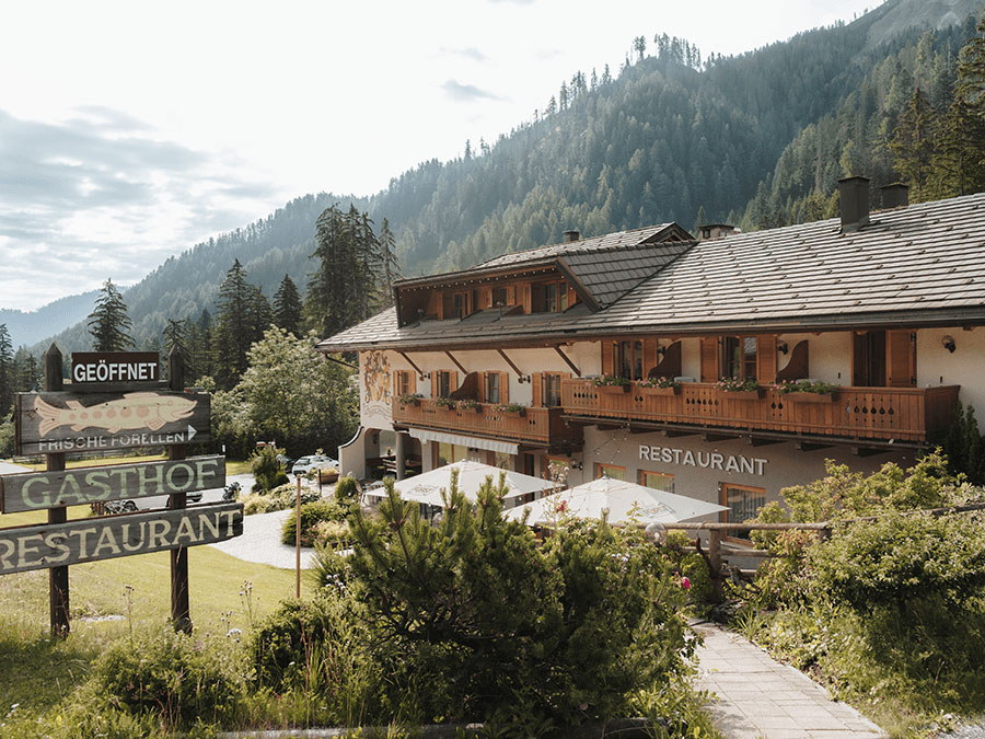 Alpines Gasthaus mit Restaurant, Holzbalkonen, Bergblick und Sitzgelegenheiten im Freien, umgeben von Bäumen. - Hotel Steinerhof