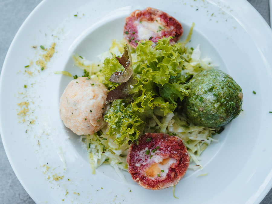 Drei bunte Teigtaschen und gemischter Blattsalat auf einem weißen Teller, darunter Salatzipfel. - Hotel Steinerhof
