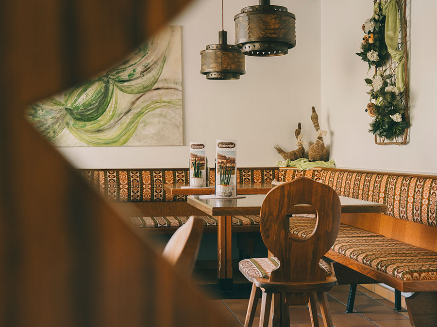 Gemütliche Café-Ecke mit gemusterten Sitzgelegenheiten, Holzstühlen und Wanddekoration, gesehen durch eine dekorative Trennwand. - Hotel Steinerhof