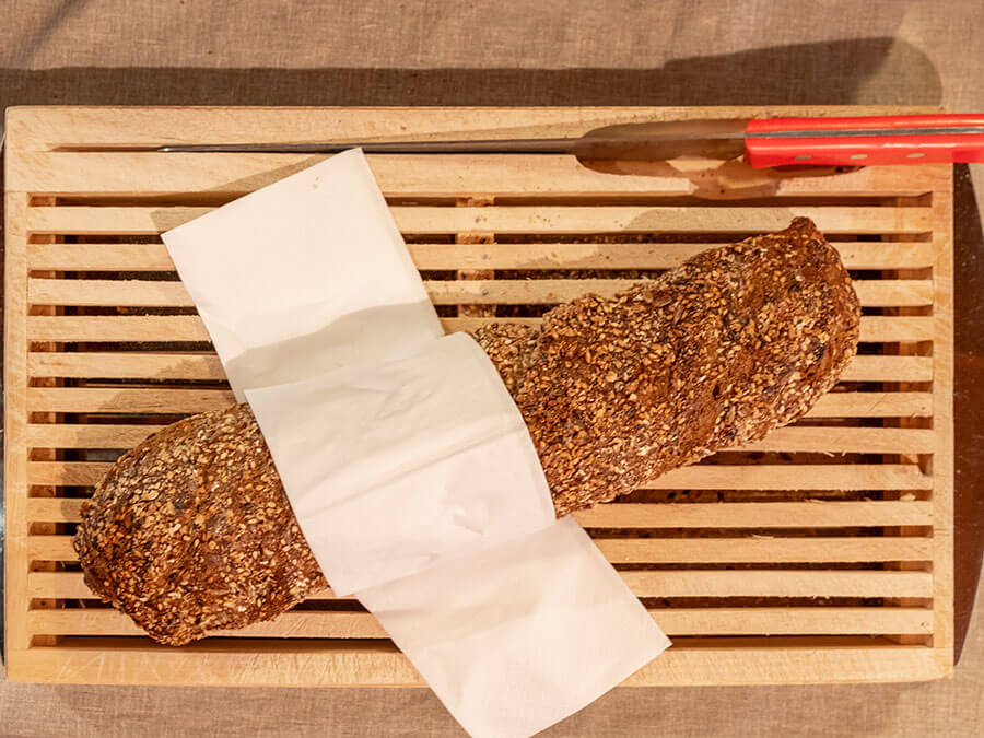 Ein Vollkornbrotlaib auf einem Holztablett, teilweise mit einer Serviette bedeckt, daneben ein Brotmesser. - Hotel Steinerhof