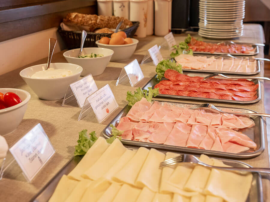Frühstücksbuffet mit Käsescheiben, Schinken, Salami, Brot, Eiern sowie Schüsseln mit Joghurt und Gemüse. - Hotel Steinerhof