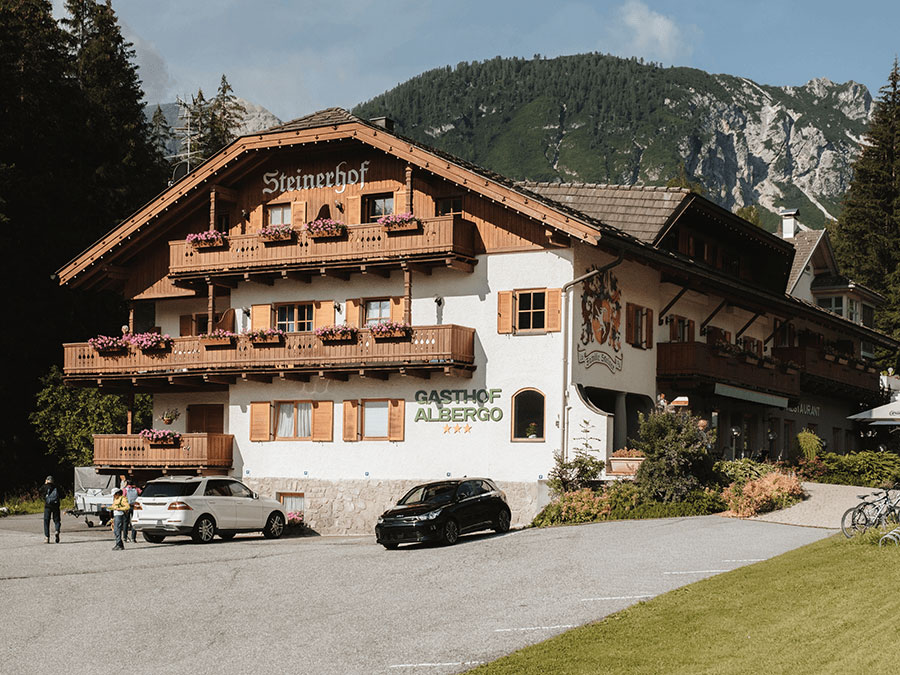 Ein Hotel im Chalet-Stil mit Blumenkästen, vor dem Haus geparkten Autos und Bergen im Hintergrund. - Hotel Steinerhof