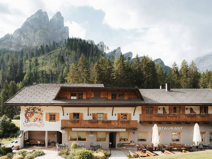 Alpenhotel mit Holzbalkonen, Sitzgelegenheiten im Freien und Berggipfeln im Hintergrund. - Hotel Steinerhof